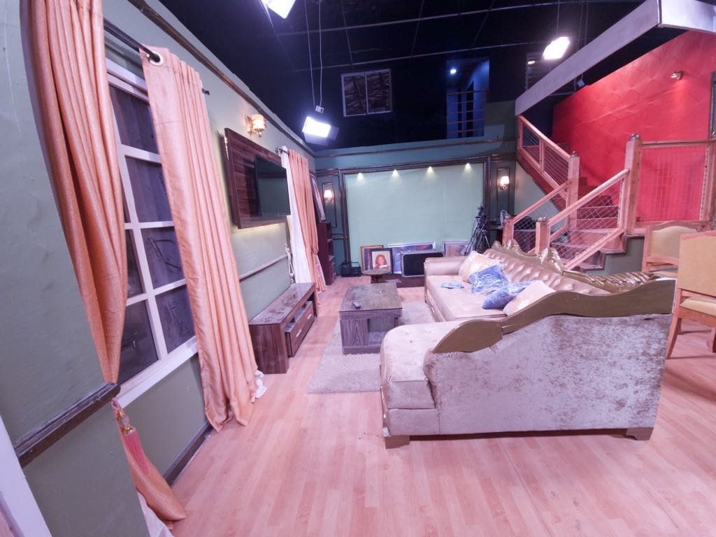 The standing house set dressed for a scene — sofas, a low table and the staircase behind